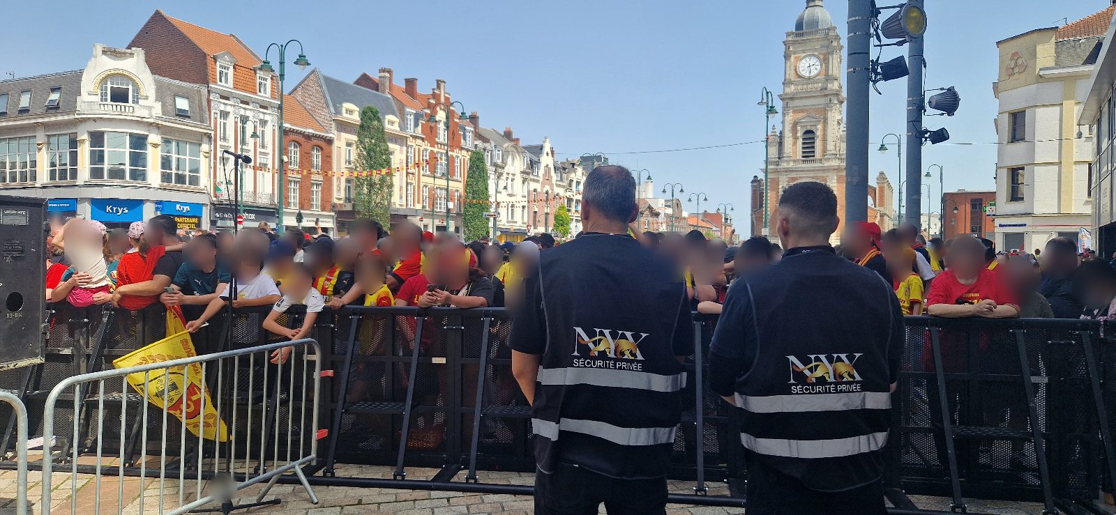 Agents NYX Sécurité Privée en gilets siglés devant la foule de supporters lensois sur la place Jean-Jaurès, beffroi de Lens en arrière-plan, lors de la fête de la Coupe de France 2026